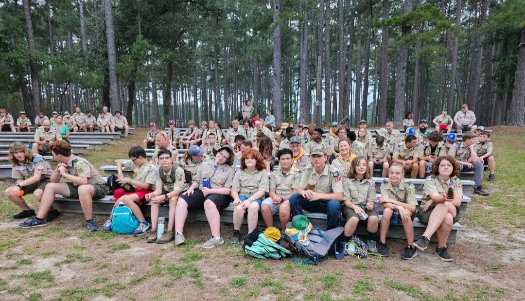 Scouts in field uniform gathered on bleachers among longleaf pines at summer camp