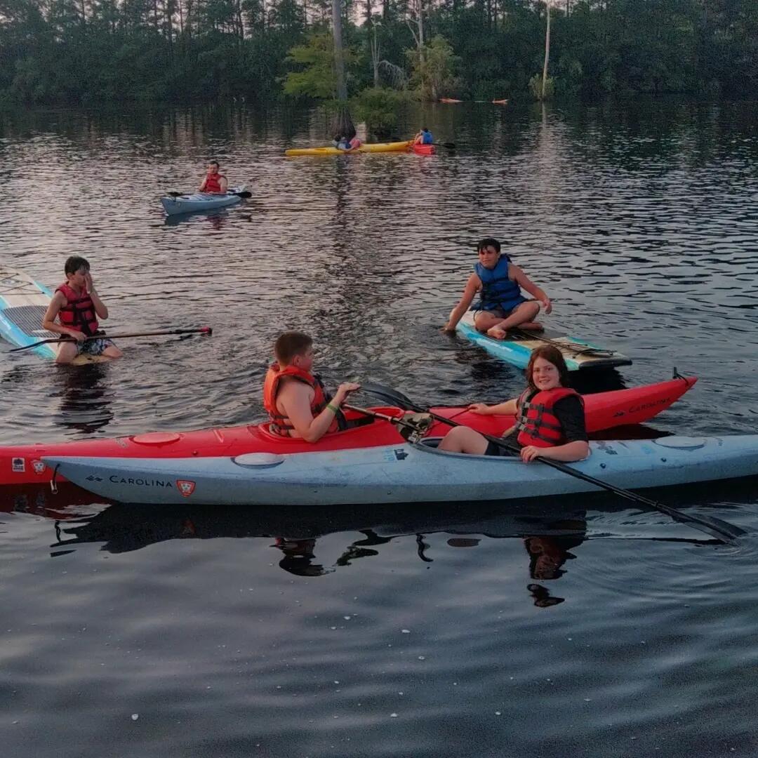 Scouts kayaking and paddleboarding on Lake Katherine at dusk during the camp beach party