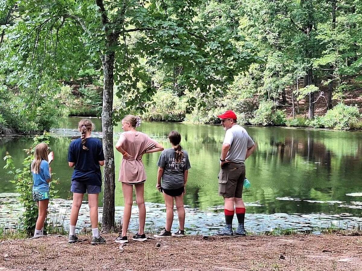 Scouts and a leader looking out over a lake at summer camp